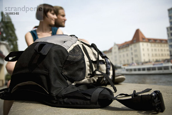 Ein Rucksack und ein junges Paar an der Spree  Berlin  Deutschland  Schwerpunkt Rucksack