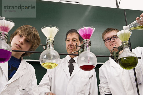Ein Lehrer  der zwei Schüler betreut  die ein Chemie-Experiment durchführen.