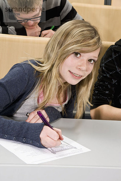 Porträt eines Teenagers  der ein Arbeitsblatt in der Klasse macht  lächelnd vor der Kamera.