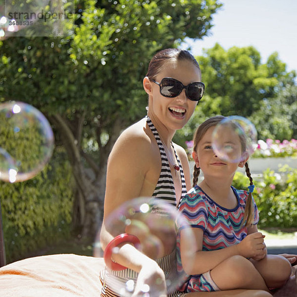 Seifenblasen  die von einer Mutter und einer Tochter  die zusammen im Freien sitzen  getragen werden.
