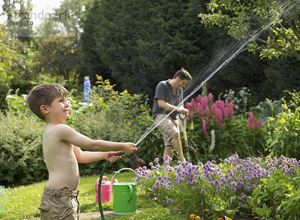 Ein Junge spritzt einen Schlauch in einen Garten.