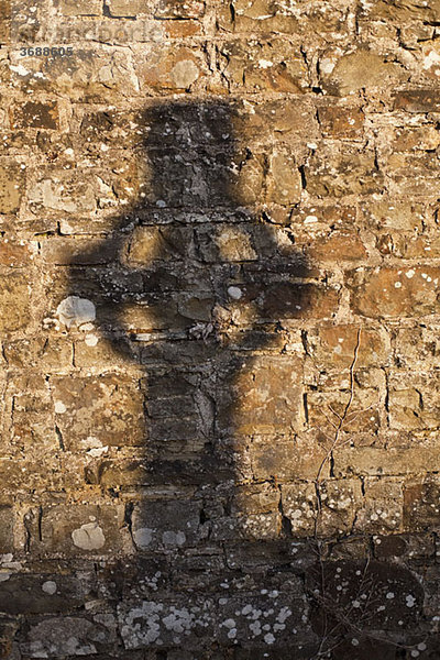 Schatten eines Kreuzes auf einer Steinmauer