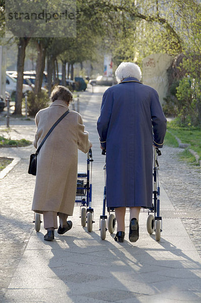 Zwei Frauen  die gemeinsam auf einem Bürgersteig gehen  Rückansicht