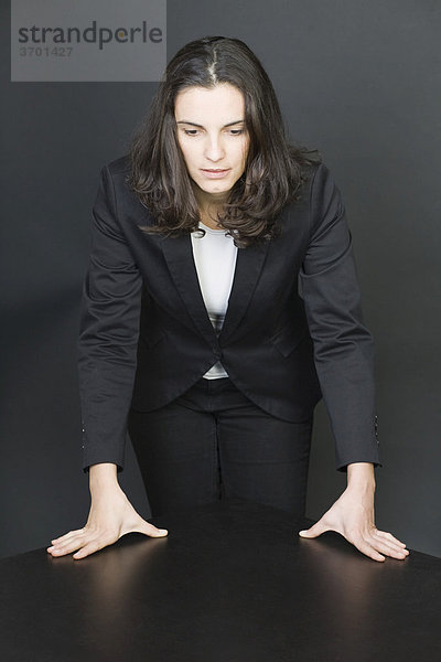 Strategie  eine Geschäftsfrau lehnt an einem schwarzen Tisch und schaut herausfordernd