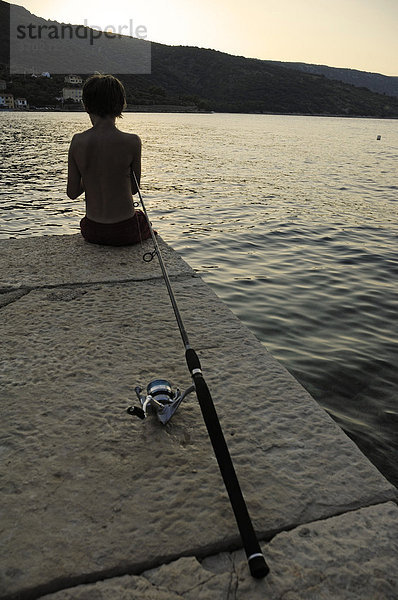 11jähriger Junge von hinten sitzt beim Angeln auf Mole  Bucht von Valun  Insel Cres  Kroatien  Europa