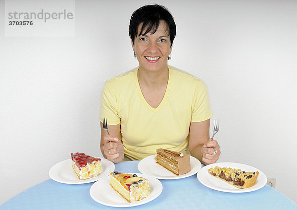 Frau sitzt zufrieden lächelnd vor vier Tellern mit Kuchen