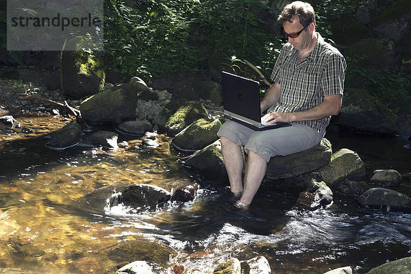 Mann  Mitte 40  sitzt an einem Bach und surft im Internet  Höllbach  Schwarzwald  Deutschland  Europa