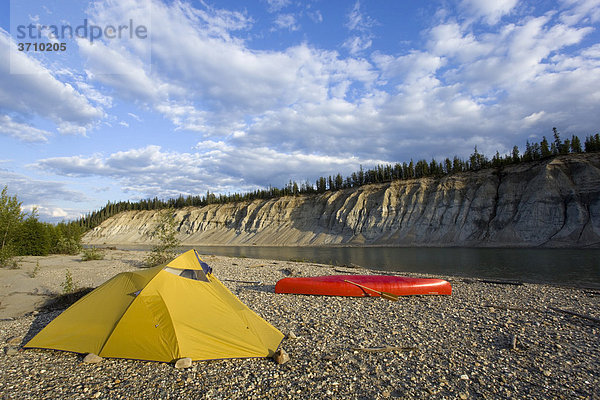 Zelt und Kanu auf einer Kiesbank  dahinter das steile Flussufer  Abendlicht  oberer Liard River Fluss  Yukon Territory  Kanada