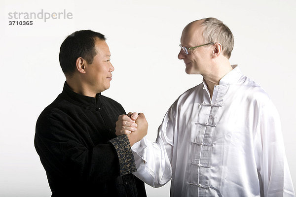 Deutsch-chinesische Freundschaft  zwei Taiji Meister reichen sich freundlich die Hände  Westeuropa trifft Asien  in traditionellen Taiji-Jacken