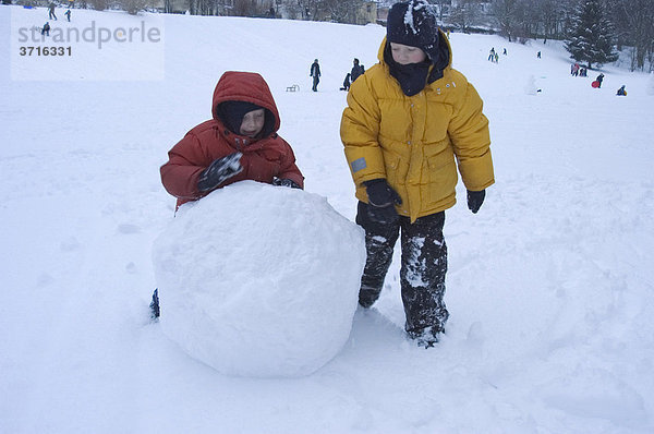 Zwei Kinder rollen große Schneekugel