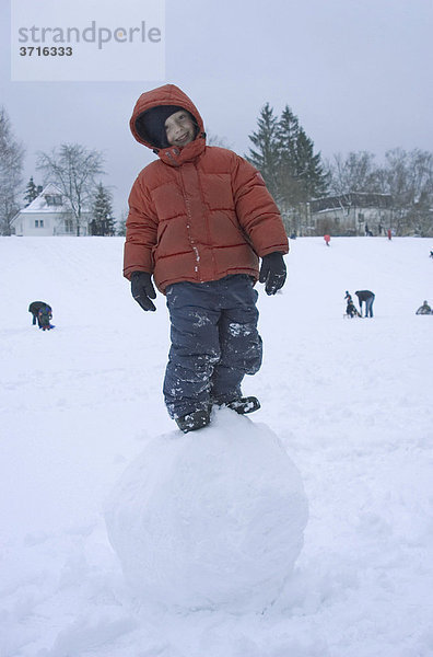 6-jähriger Junge steht auf großer Schneekugel