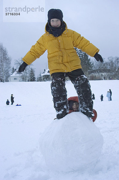 Kleiner junge schaut zwischen den Beinen durch  während der andere Junge auf der Schneekugel balanciert
