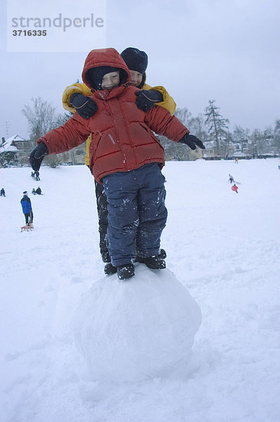 Zwei Kinder balancieren auf einer großer Schneekugel