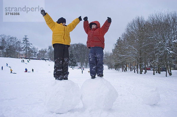 Zwei Jungen stehen auf großen Schneekugeln