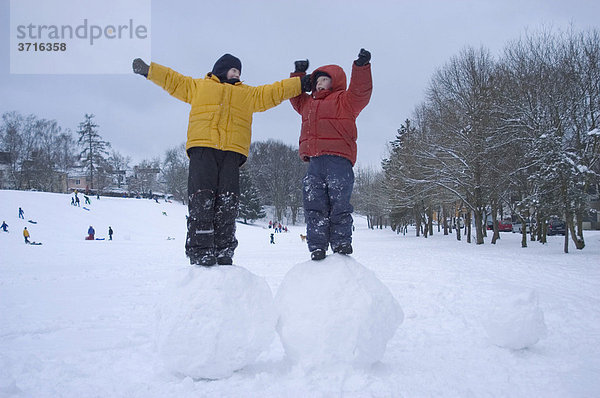 Zwei Jungen stehen auf großen Schneekugeln