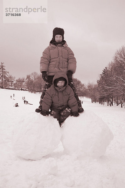 Zwei Jungen auf großen Schneekugeln