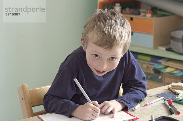 Sechsjähriger Junge sitzt am Schreibtisch beim Hausaufgaben machen