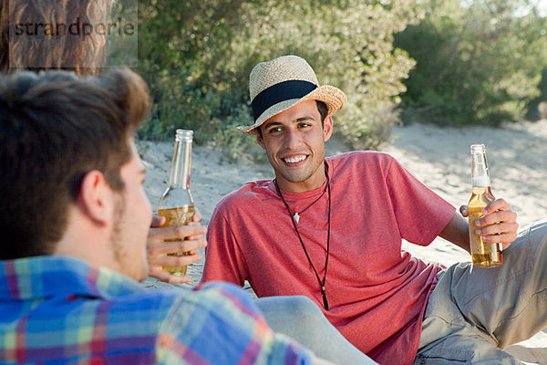 Jungen Freunde sitzen auf Sand mit Bier