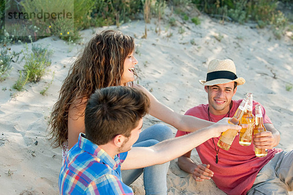 Junge Freunde sitzen auf Sand mit Bier