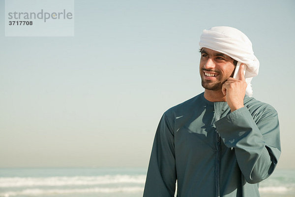 Mann aus dem Nahen Osten mit Handy am Strand