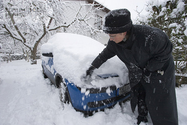 Eingeschneites Auto Opel Corsa blau - Frau beseitigt Schnee vom Auto