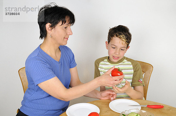 Frau reicht ihrem Kind eine Tomate zur Zubereitung eines Salates