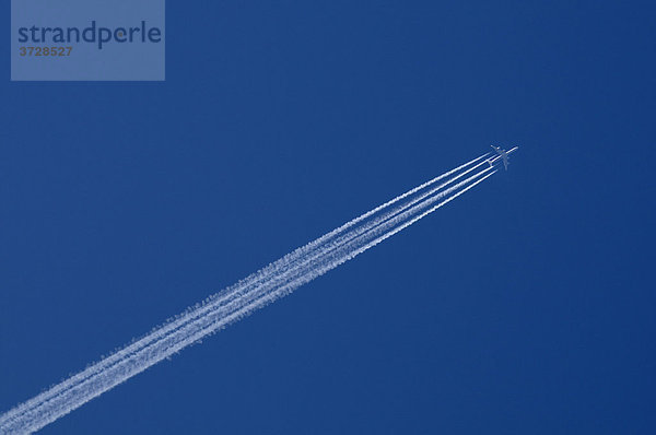 Vierstrahliges Flugzeug zieht Kondensstreifen über stahlblauen Himmel