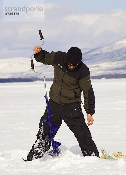 Mann beim Eisfischen  bohrt ein Loch mit einem Eisbohrer  Fox Lake  Yukon Territory  Kanada