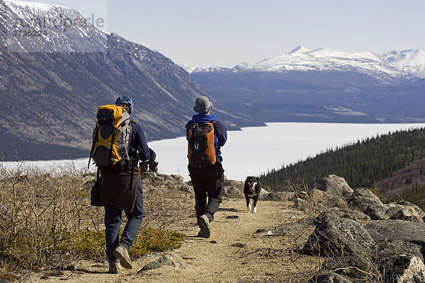 Wandergruppe mit Rucksäcken vor dem vereisten Kusawa See und Bergen  Yukon Territory  Kanada  Nordamerika