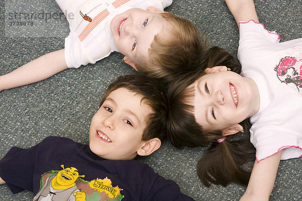 Drei Kinder  6  3 und 7 Jahre  liegen auf Teppich