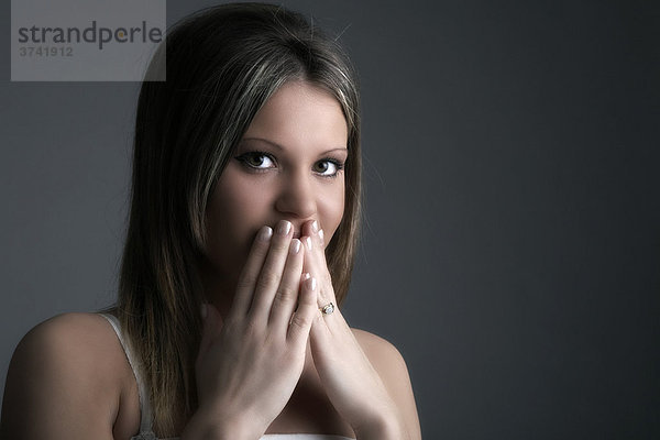Junge Frau hält verschämt ihre Hände vor den Mund