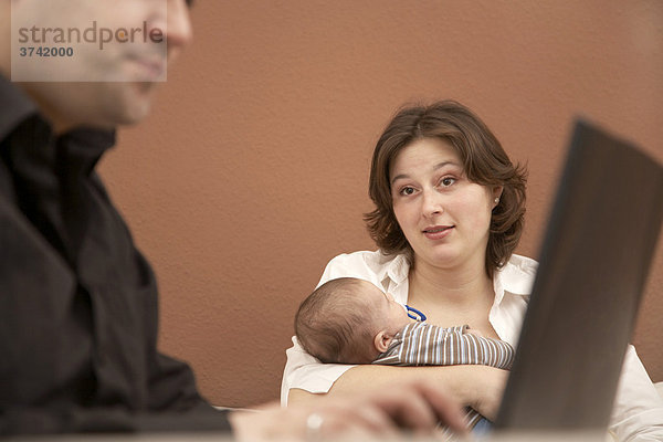 Ehemann arbeitet am Computer während die junge Mutter entnervt blickt