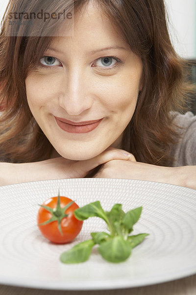Junge Frau mit einzelner Tomate und Salat auf ihrem Teller