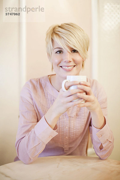 Junge Frau mit kurzen blonden Haaren trinkt Kaffee