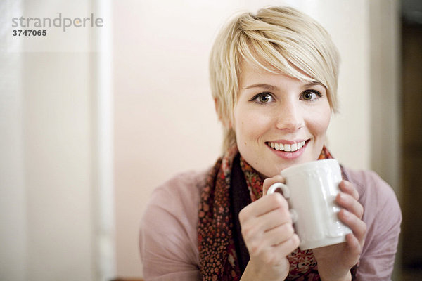 Junge Frau mit kurzen blonden Haaren trinkt Kaffee