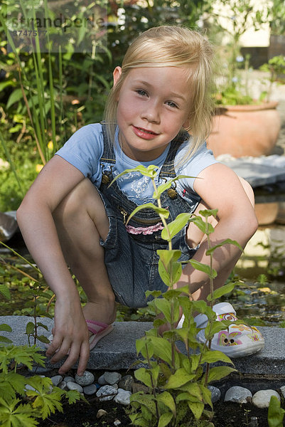 Mädchen  5 Jahre  mit unterschiedlichen Schuhen  sitzt vor einem Gartenteich