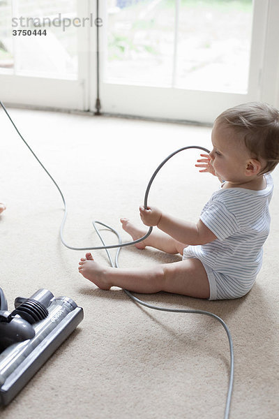 Baby auf dem Boden spielend mit Staubsaugerkabel