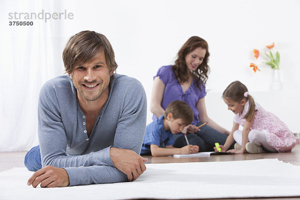 Lächelnder Mann auf Teppich Familie im Hintergrund