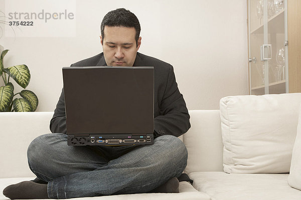 Junger Mann sitzt vor seinem Laptop auf dem Sofa