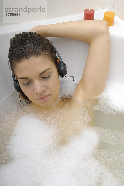 Dunkelhaarige Frau in der Badewanne hört Musik mit Kopfhörern