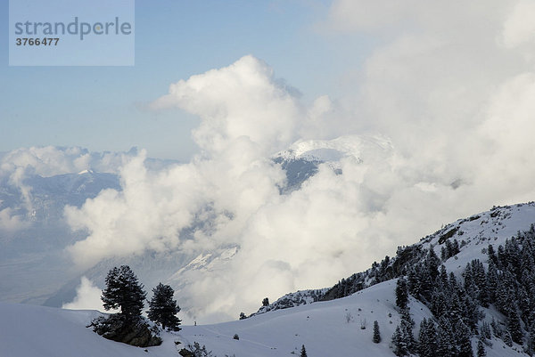 Aufteigende Nebelschwaden eines abziehenden Tiefdruckgebietes zieht über verschneite Berghänge Tirol Österreich