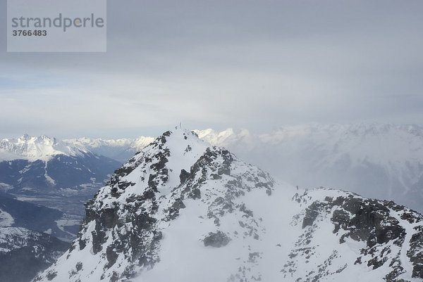 Verschneiter Berggipfel mit Gipfelkreuz und Bergsteiger über dem Inntal bei starkem Föhnsturm  Tuxer voralpen Tirol Österreich