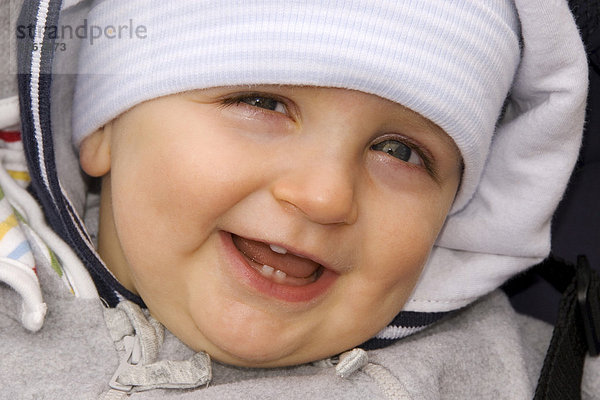 Kleiner Junge  10 Monate  mit dicker Jacke und Mütze lacht  Deutschland