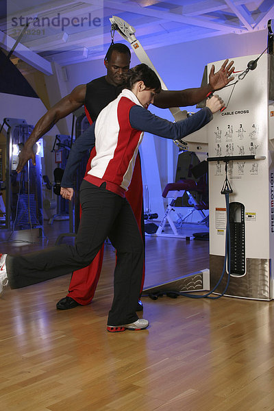 Fitnesstrainer übt mit einer jungen Frau an einer Seilzugmaschine in einem Sportstudio