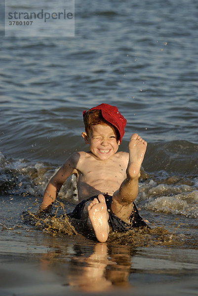 Kleiner junge sitzt am Strand und planscht mit dem Wasser