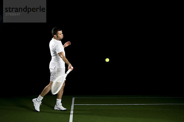 Ein Tennisspieler im Begriff  einen Ball zu schlagen  Studioaufnahme  Porträt