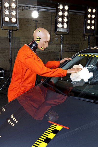 Ein Crashtest-Dummy  der die Windschutzscheibe eines Crashtestautos wäscht.