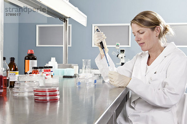 Ein Labortechniker  der eine Probe mit einer Pipette in ein Fläschchen gibt.