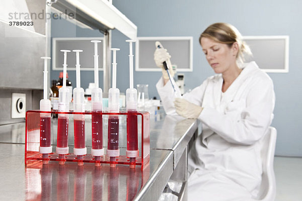 Eine Reihe von Fläschchen mit Blut und ein Laborant  der im Hintergrund arbeitet  konzentrieren sich auf den Vordergrund.