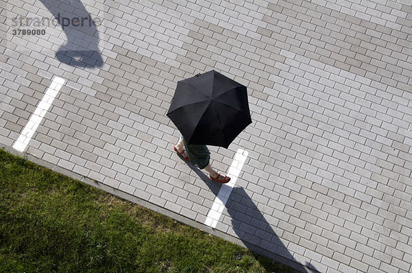 Eine Frau  die durch einen Platz läuft und einen Regenschirm hält.